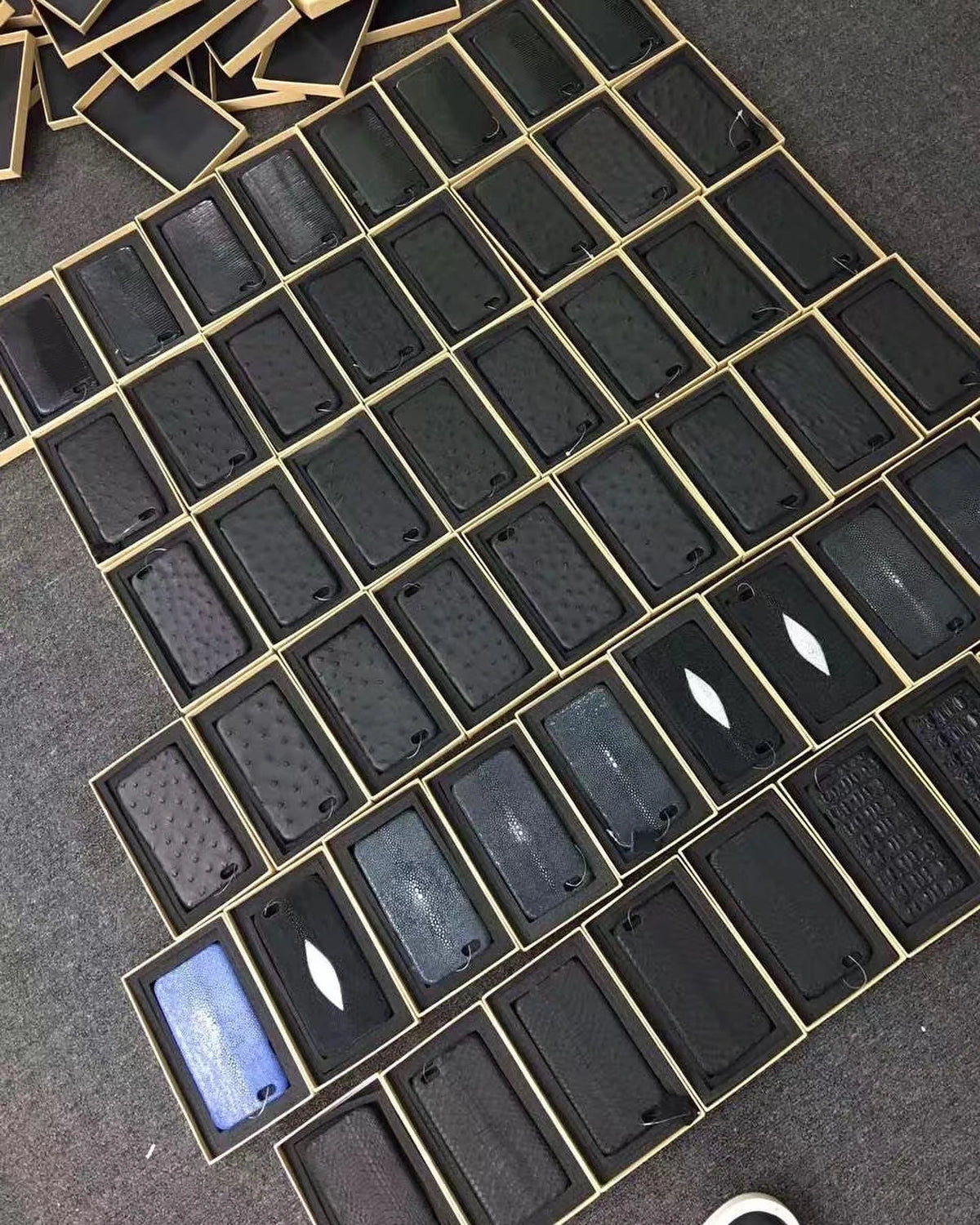 A batch of finished exotic leather phone cases arranged in presentation boxes
