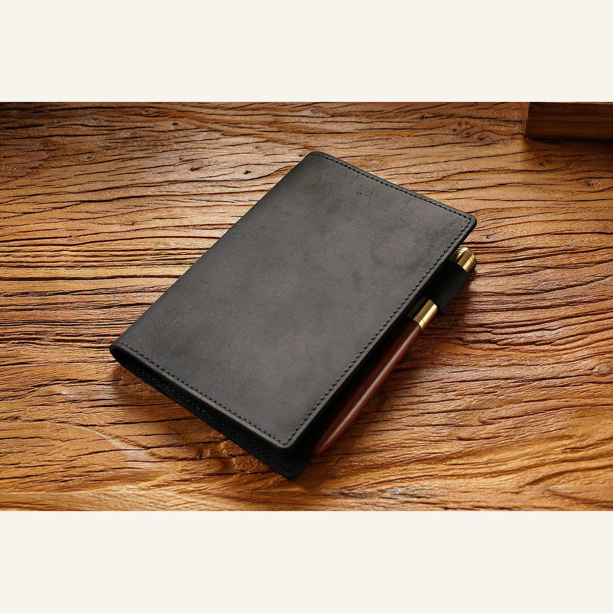 Black leather notebook cover with refill and pens on a wooden desk