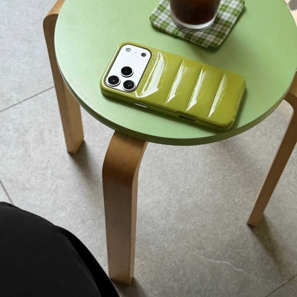 Mustard-green puffer-style phone case shown on a display phone in a table setting.