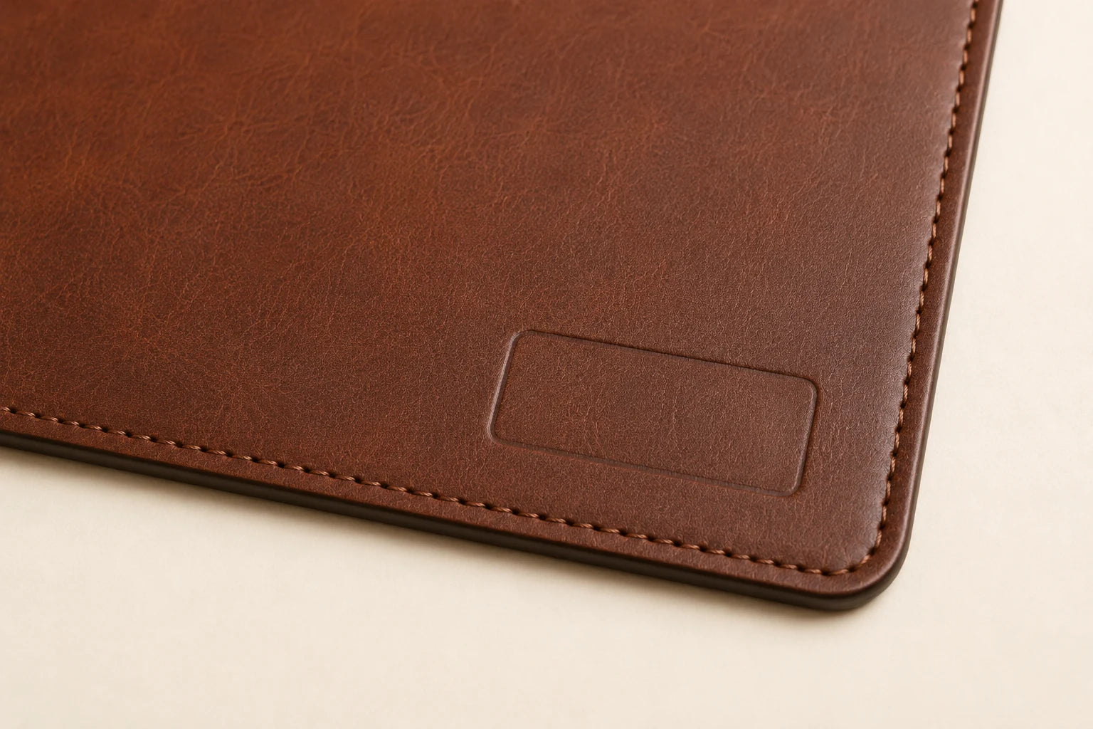 Macro detail of blank debossing area and stitched edge on brown leather desk mat