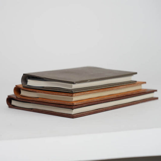 Stacked refillable leather book covers in brown and gray color options