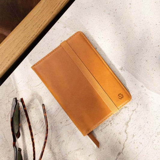 Tan leather passport cover with elastic band on a tabletop